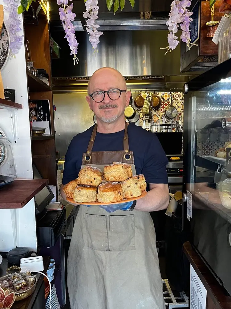 Baker holding a plate of homemade scones beside Truva Coffee Roasters bags