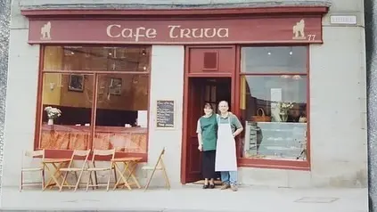Faded photograph of the original Cafe Truva shopfront in the late 1990s with two people at the door